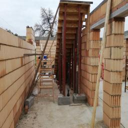 AGBUD KAROL MANIA - Wnętrze budowanego domu z czerwonej cegły ceramicznej, widoczne podpory stropowe, drabina i narzędzia budowlane.