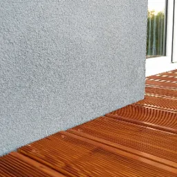 Nowoczesny taras z drewna egzotycznego, deski ryflowane, szara ściana z tynkiem strukturalnym i białe okno tarasowe.