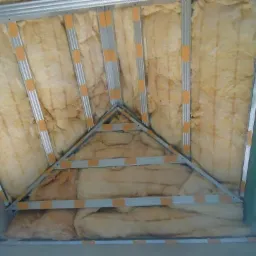 Izolacja poddasza wełną mineralną, widoczne profile metalowe mocowane taśmą, surowy stan przed wykończeniem.