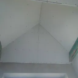 Skośne poddasze z zamontowanymi płytami gipsowo-kartonowymi, widoczne drewniane belki konstrukcyjne, połączenia płyt uszczelnione, przygotowane do dalszych prac wykończeniowych.