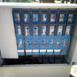 Otwarta skrzynka elektryczna z widocznymi bezpiecznikami i przewodami, zamontowana na zewnątrz budynku.