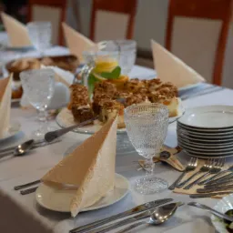 Uroczysty stół z białym obrusem, zastawą, deserem i napojami. Eleganckie nakrycie, dekoracyjne serwetki i szklanki. Przygotowania do przyjęcia.