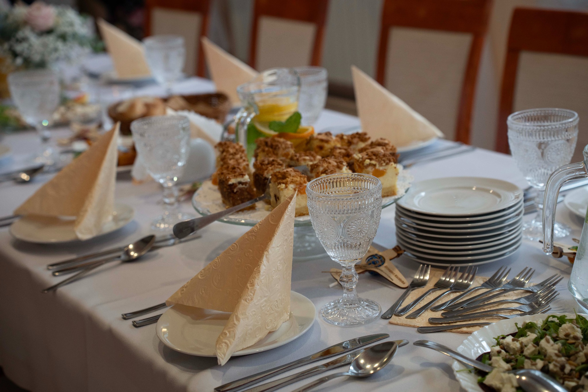 Uroczysty stół z białym obrusem, zastawą, deserem i napojami. Eleganckie nakrycie, dekoracyjne serwetki i szklanki. Przygotowania do przyjęcia.