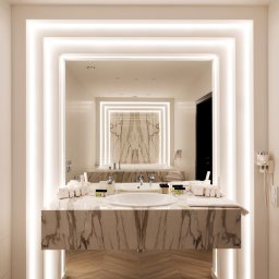 Katarzyna Gruca PROJEKTOWANIE - Elegancka łazienka z marmurowym blatem umywalki, podświetlanym lustrem w geometrycznej ramie i drewnianą podłogą ułożoną we wzór jodełki.