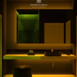 Nowoczesna łazienka z podświetlanym lustrem, czarną umywalką nablatową i zielonym akcentem w kabinie prysznicowej, uzupełniona okrągłym pufem i drewnianą podłogą.