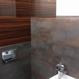 Nowoczesna łazienka z brązowymi płytkami imitującymi drewno i szarymi kaflami, biała umywalka z chromowaną baterią oraz toaleta wisząca z przyciskiem spłukującym.