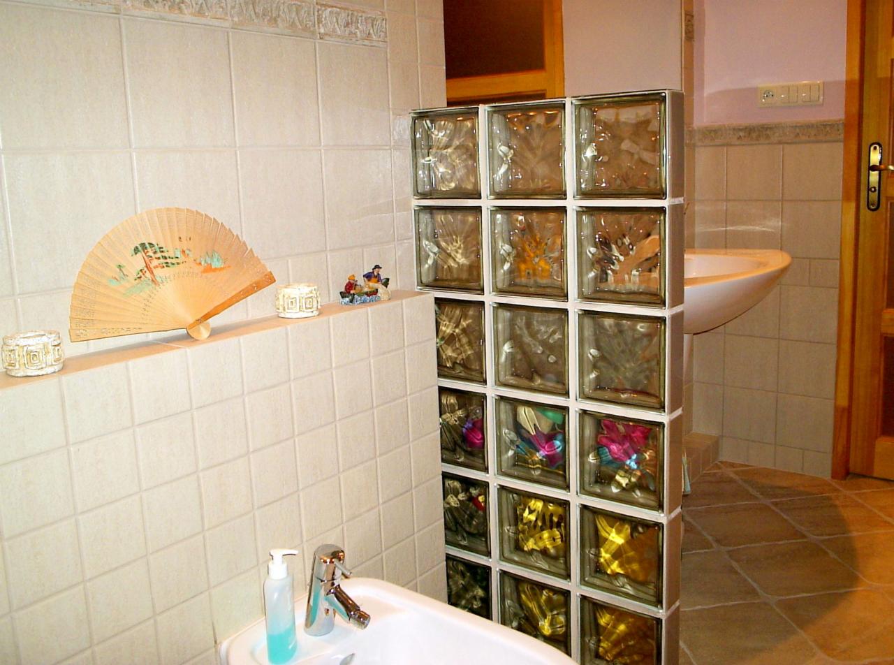 Ścianka działowa z luksferów w łazience z beżowymi płytkami, widoczny fragment umywalki i dekoracje na półce.