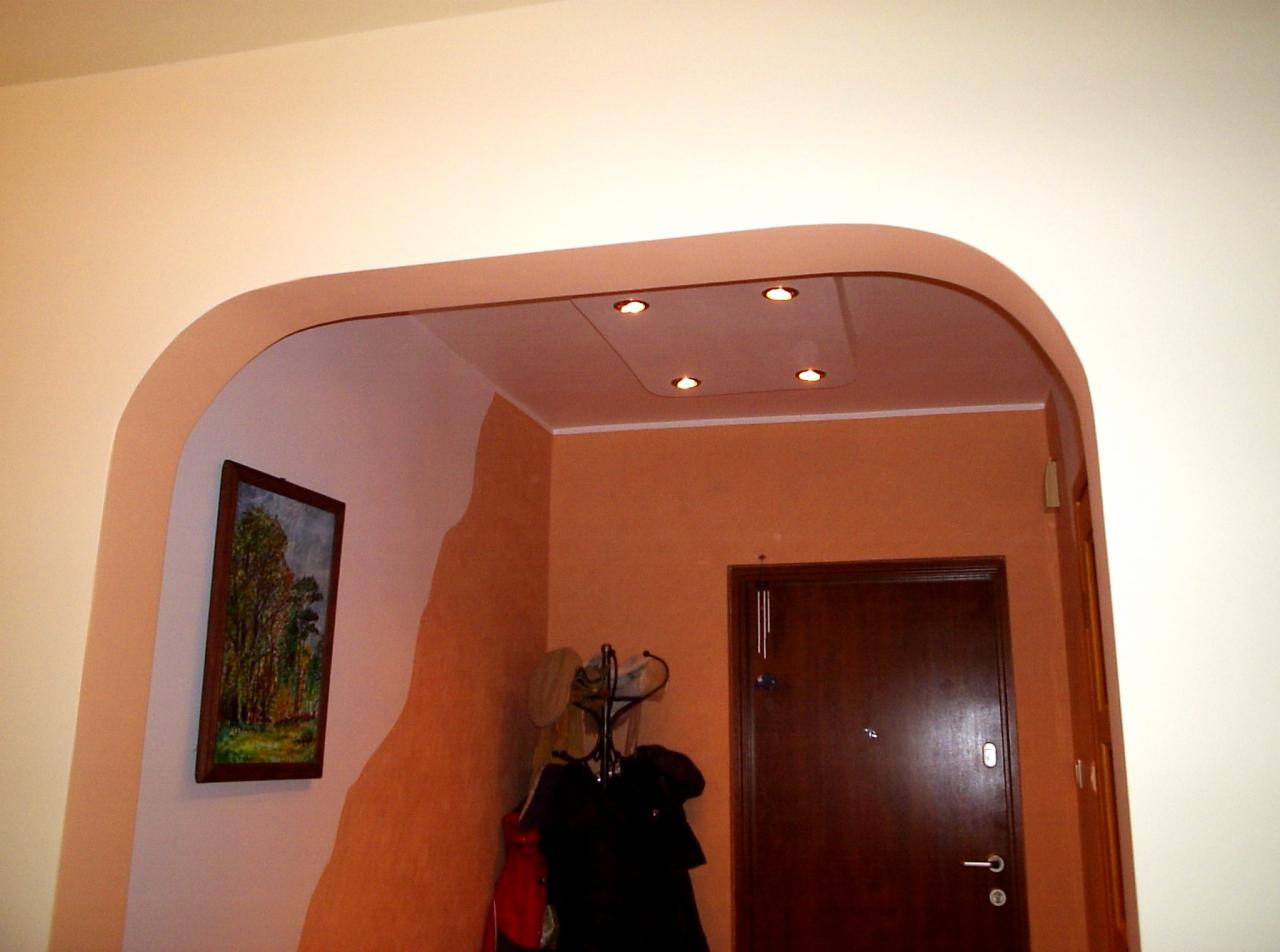 Aranżacja przedpokoju z łukowatym przejściem, oświetleniem punktowym w suficie podwieszanym i obrazem na ścianie z dekoracyjnym malowaniem.