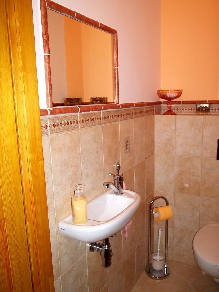 Mała łazienka w beżowych płytkach z wiszącą umywalką, lustrem w ozdobnej ramie i toaletą.