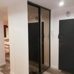 Wnętrze mieszkania z zamontowaną szafą wnękową z przesuwnymi, lustrzanymi drzwiami i widocznymi narzędziami na podłodze.