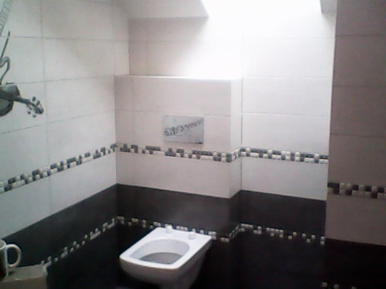 Nowoczesna łazienka z białymi i ciemnobrązowymi płytkami, dekoracyjnym pasem płytek mozaikowych, podwieszaną toaletą i widocznym fragmentem dekoracji ściennej w kształcie gitary.