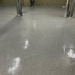 MP SYSTEM Piotr Marciniak - Błyszcząca, szara posadzka z drobnymi, ciemnymi plamkami w przestronnym garażu z podnośnikami samochodowymi. Gładka powierzchnia, widoczne odbicia światła.