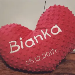 Czerwona poduszka w kształcie serca z wytłaczaną fakturą, haftowanym imieniem 'Bianka' i datą '05.12.2017r.'