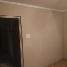 Świeżo otynkowane ściany w pokoju z widocznym wejściem do innego pomieszczenia, listwa dekoracyjna przy suficie.