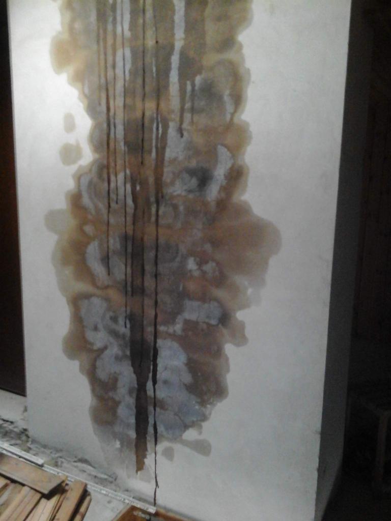 Zacieki wodne na ścianie, widoczne ślady wilgoci i pleśni, uszkodzona powierzchnia ściany.