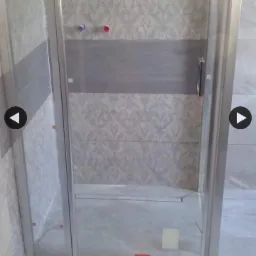 Nowoczesna kabina prysznicowa z przesuwnymi drzwiami, wykończona szarymi płytkami z dekoracyjnym wzorem i poziomym pasem, widoczne przyłącza wodne.