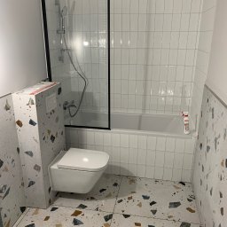 Specdom - Wykończona łazienka z białą armaturą i płytkami lastryko na podłodze i ścianach. Kabina prysznicowa z czarną ramą i białe, prostokątne płytki na ścianach w strefie kąpieli.