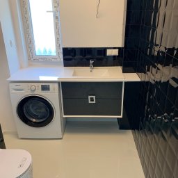 Specdom - Nowoczesna łazienka po remoncie: białe płytki podłogowe, czarne, błyszczące płytki na ścianie, pralka Samsung obok umywalki z szafką. Okno z widokiem na zieleń.