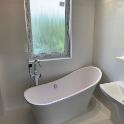 Specdom - Nowoczesna, jasna łazienka po remoncie: wolnostojąca wanna, umywalka i okno z widokiem na zieleń. Białe płytki na ścianach i podłodze. Minimalistyczny styl.