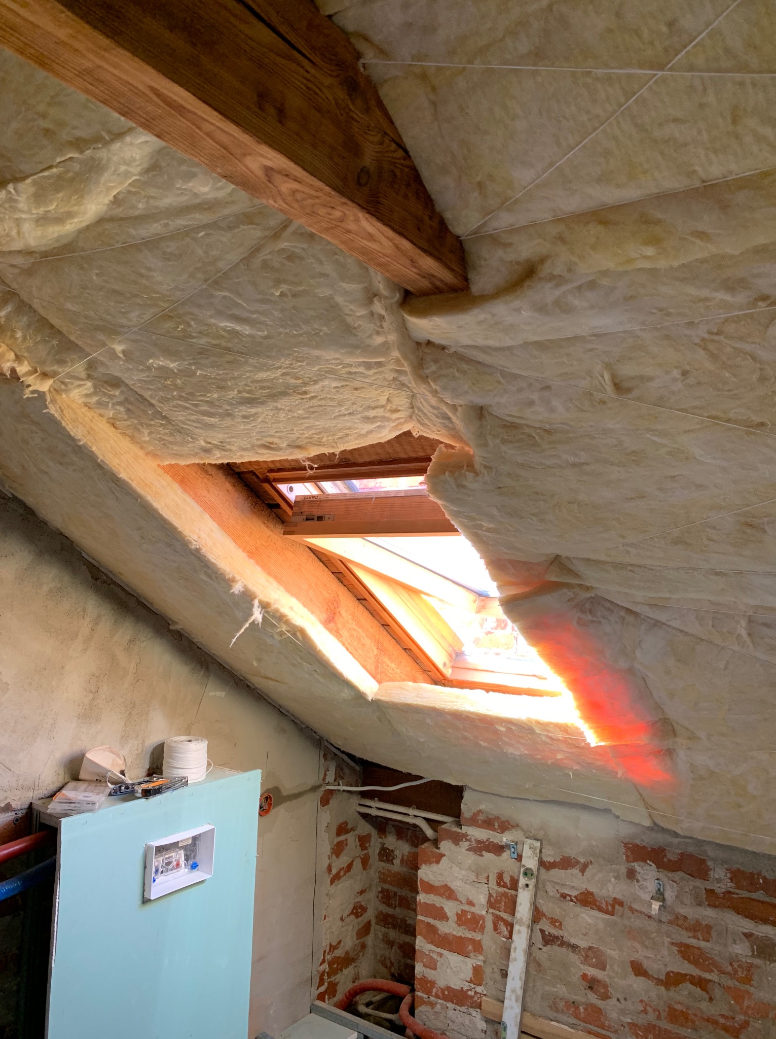 Ocieplenie poddasza wełną mineralną z oknem dachowym, widoczne elementy konstrukcyjne i instalacje w trakcie prac w Wrocławiu. Izolacja termiczna dachu.