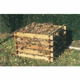 Drewniany kompostownik wypełniony opadłymi liśćmi, ustawiony na trawie w ogrodzie, widoczne elementy konstrukcyjne z surowego drewna.