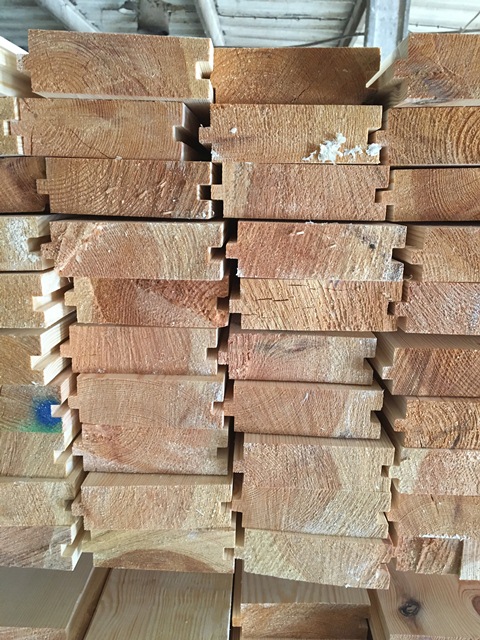 Stos desek podłogowych z widocznymi połączeniami wpustowymi, ułożonych równo w magazynie.