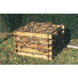 Drewniany kompostownik wypełniony opadłymi liśćmi, ustawiony na trawie w ogrodzie, widoczne elementy konstrukcyjne z surowego drewna.