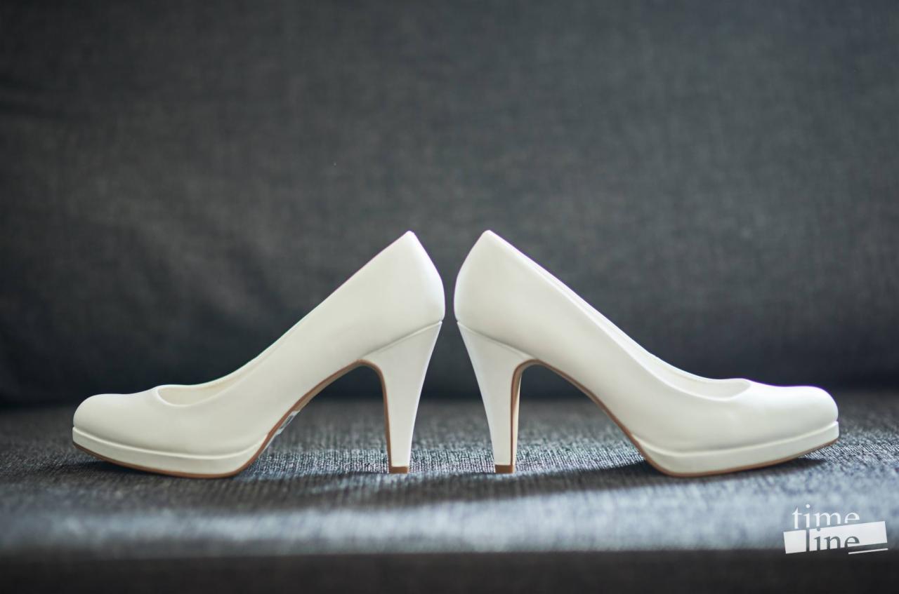 Dwa białe, skórzane czółenka ślubne na platformie, ustawione pod kątem na szarym tle. Widoczne brązowe podeszwy i smukłe obcasy.
