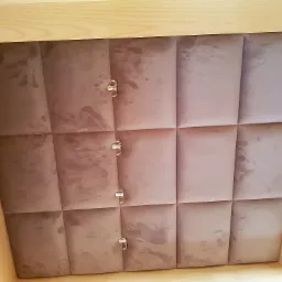 Tapicerowany panel ścienny w odcieniach różu z trzema ozdobnymi, srebrnymi haczykami, zamontowany w drewnianej wnęce.