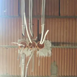 Widok na trzy pomarańczowe puszki instalacyjne osadzone w czerwonej cegle dziurawce, z których wystają białe przewody elektryczne; widoczne napisy na przewodach.