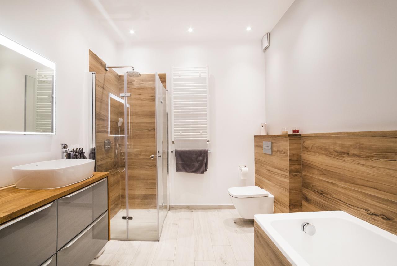 Nowoczesna łazienka z kabiną prysznicową w stylu drewna, umywalką nablatową na szafce z szufladami w kolorze szarym oraz białymi płytkami podłogowymi.