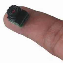 Miniaturowa kamera szpiegowska umieszczona na opuszku palca, ukazująca jej niewielkie rozmiary.