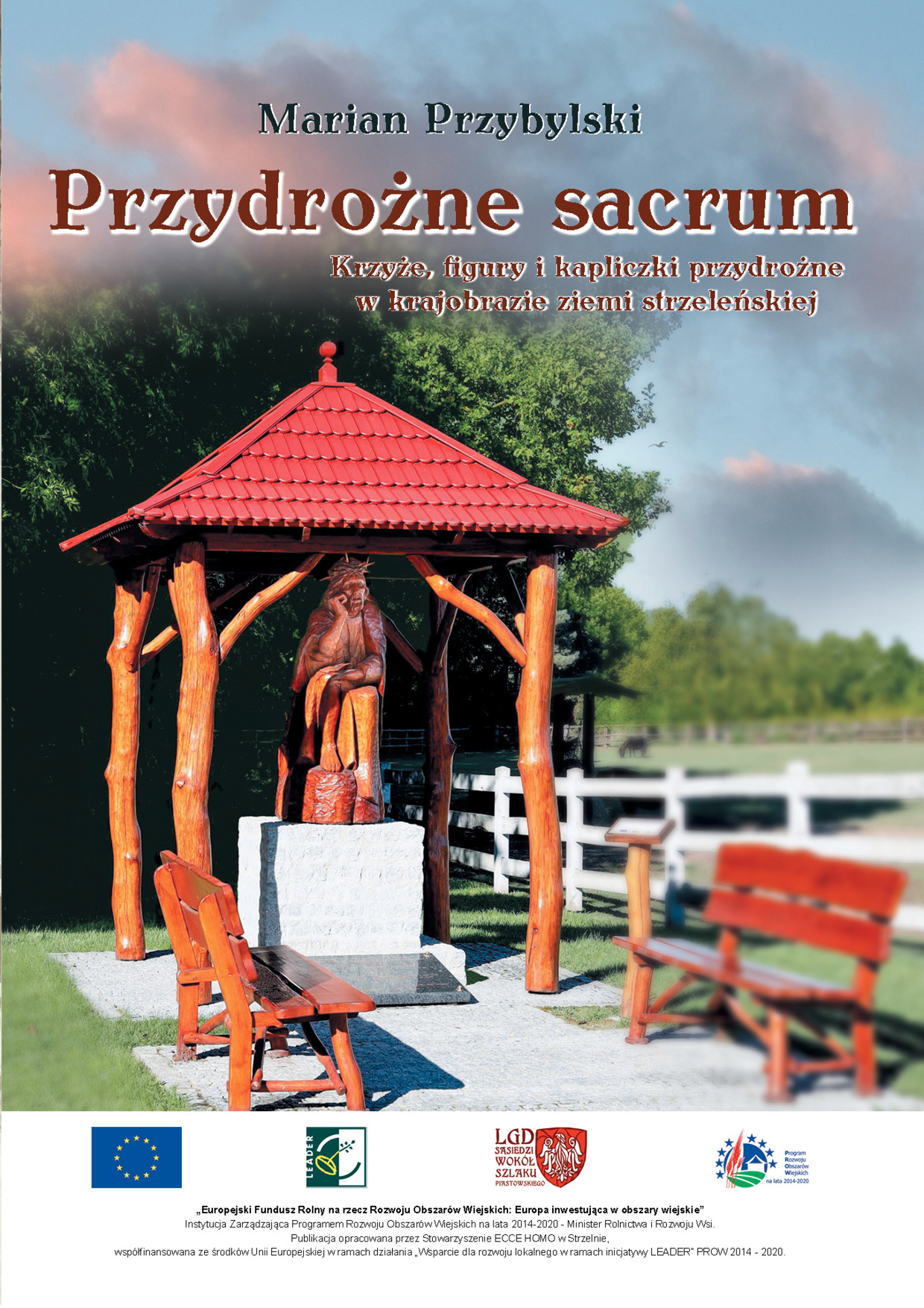 Okładka książki 'Przydrożne sacrum' Mariana Przybylskiego, przedstawiająca drewnianą kapliczkę z rzeźbą Jezusa w koronie cierniowej, z czerwonym dachem i ławkami na tle zieleni i białego płotu.