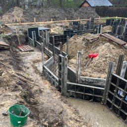 Budowy-Remonty Robert Niewiadomski - Wykop pod fundamenty domu z użyciem szalunków systemowych, widoczny zielony kubeł z narzędziami i pryzma ziemi w tle.