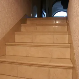 Schody wyłożone beżowymi płytkami ceramicznymi z zaokrąglonymi krawędziami, widok z dołu, ściana z fakturą baranka.