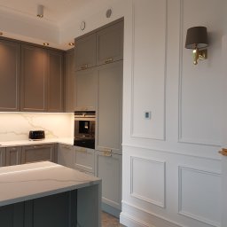 WOJCIECH ROCIEK CONTRACTOR - USŁUGI STOLARSKIE - Nowoczesna kuchnia w odcieniach szarości z wyspą i białymi ścianami z dekoracyjnymi panelami, oświetlona punktowo i kinkietem.