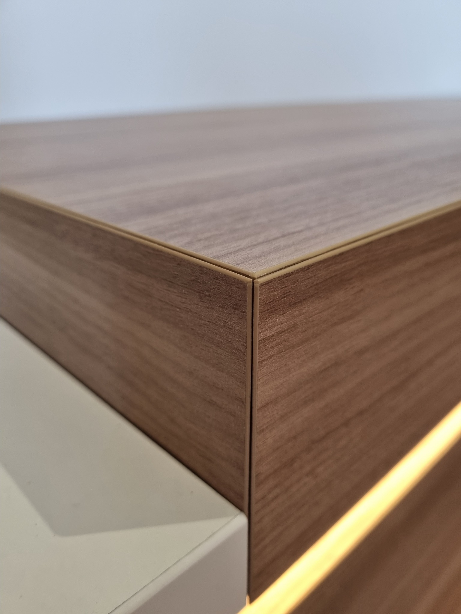 Detale narożnika szafki z drewnopodobnym fornirem, oświetlenie LED wzdłuż krawędzi, biały element pod spodem, precyzyjne łączenie elementów.