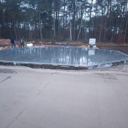 HEXIUM SPÓŁKA Z OGRANICZONĄ ODPOWIEDZIALNOŚCIĄ - Wylany fundament pod budowę domu, widoczne ślady po pracy ekipy budowlanej. W tle las i przygotowany teren pod inwestycję.