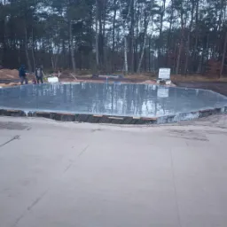 Wylany fundament pod budowę domu, widoczne ślady po pracy ekipy budowlanej. W tle las i przygotowany teren pod inwestycję.