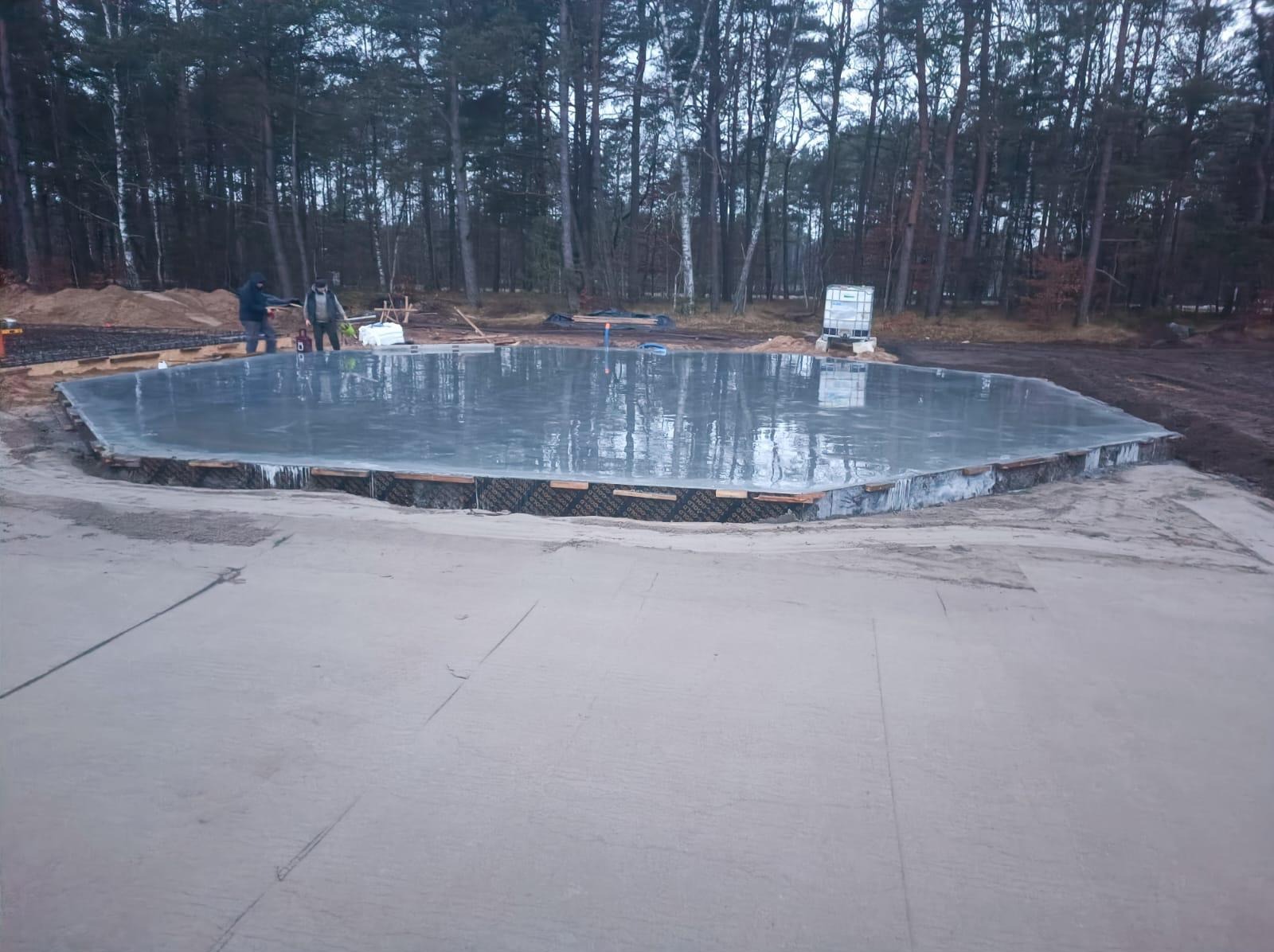 Wylany fundament pod budowę domu, widoczne ślady po pracy ekipy budowlanej. W tle las i przygotowany teren pod inwestycję.