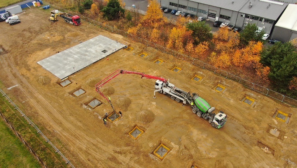 Betonowanie fundamentów punktowych z użyciem pompy do betonu. Widok z góry na plac budowy z wykopami i częściowo zalaną płytą fundamentową.
