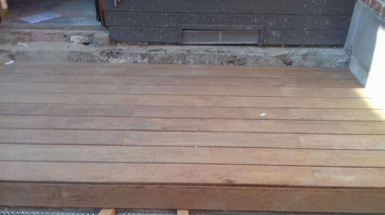 Nowy drewniany taras ułożony przed wejściem do budynku, widoczne deski tarasowe i elementy konstrukcyjne pod spodem.