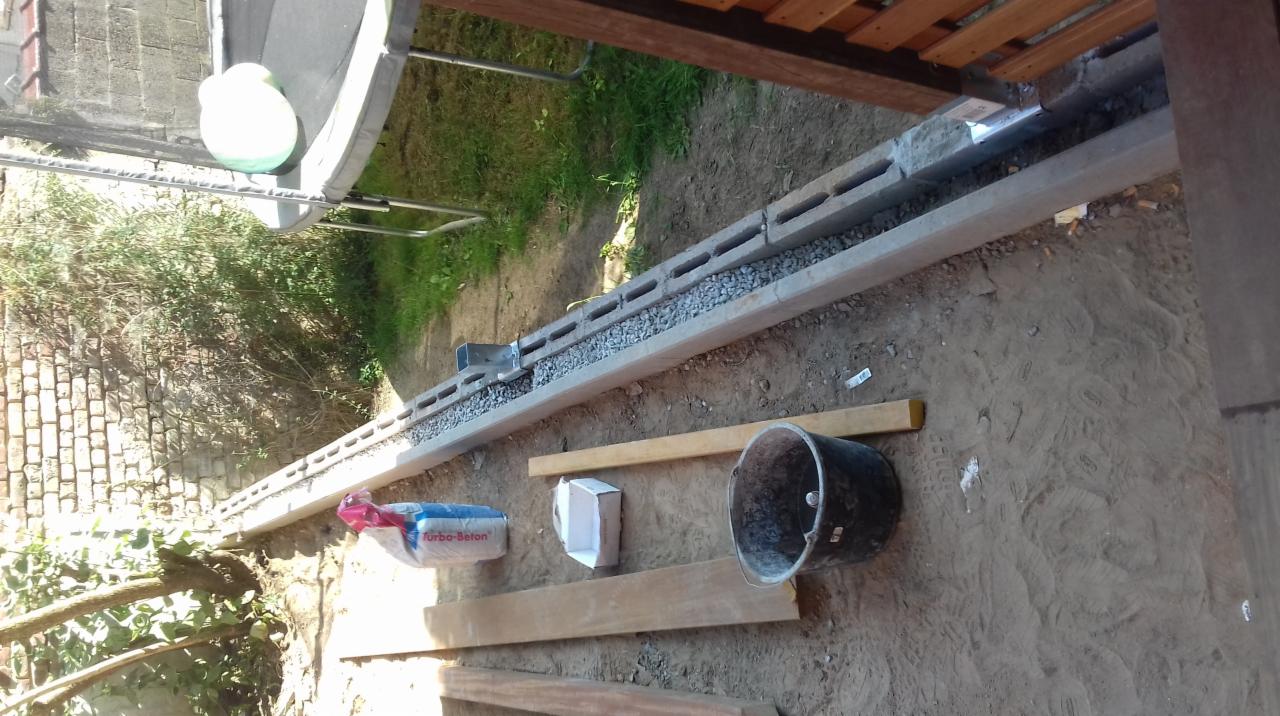 Budowa fundamentu: bloczki betonowe wypełnione żwirem, widoczny worek z betonem, kubeł i drewniane deski na ziemi.