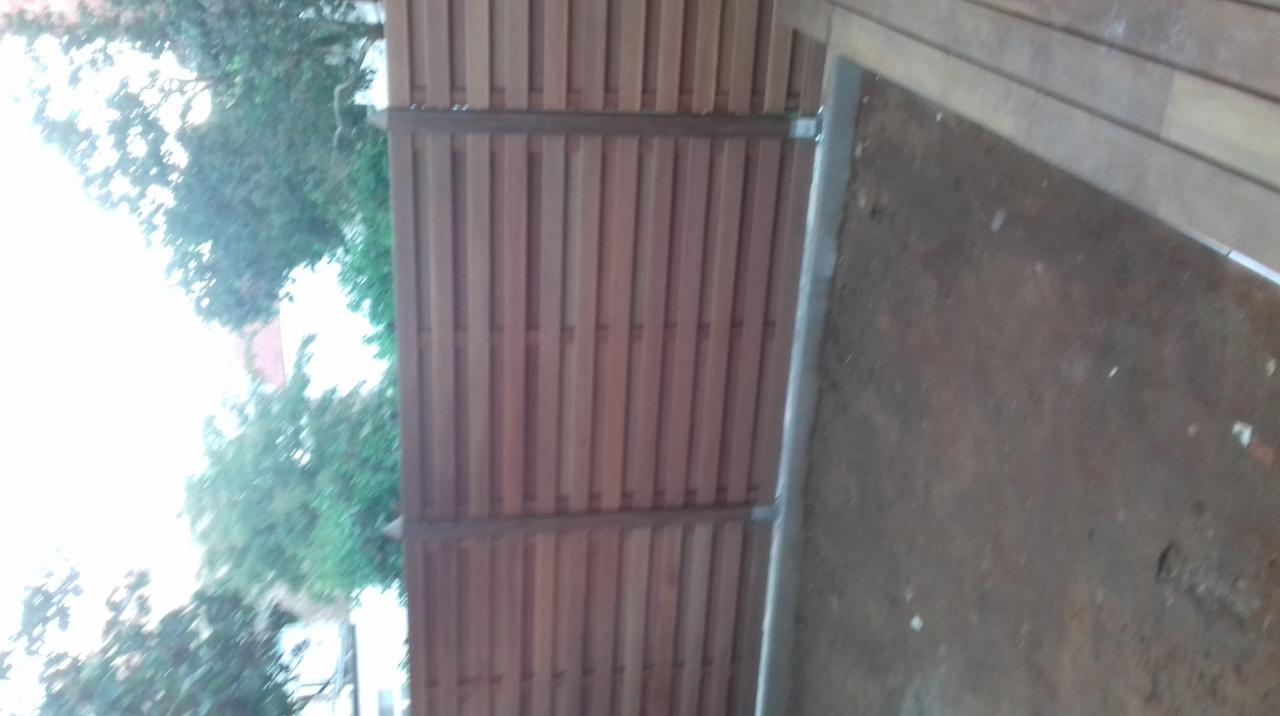 Drewniany płot z metalowymi słupkami, widok z góry na częściowo wyłożony drewnem taras i zieleń w tle.