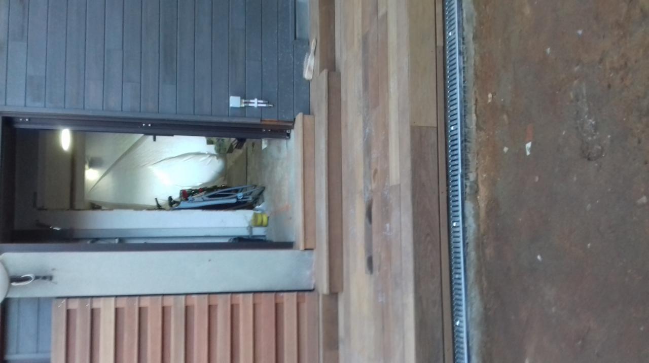 Montaż okna z drewnianą ramą; widoczna folia ochronna wewnątrz pomieszczenia, drewniana podłoga i listwa odpływowa