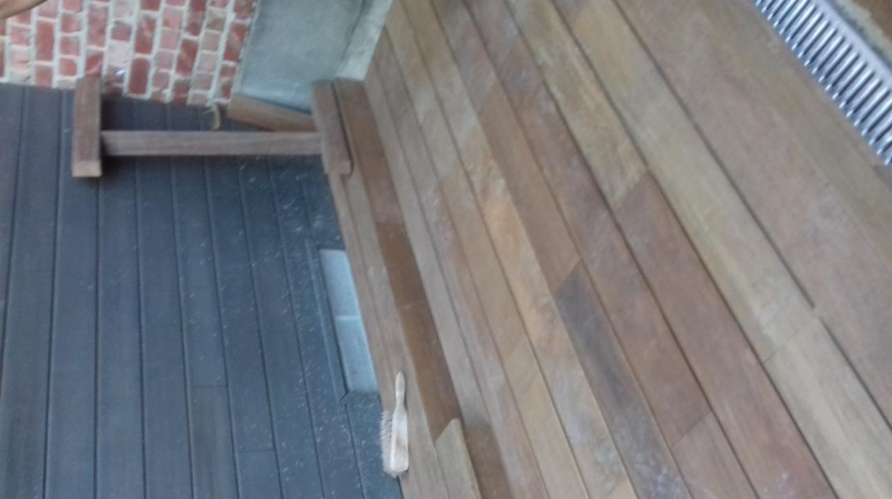 Ułożony taras z desek kompozytowych w dwóch odcieniach brązu, z widocznym fragmentem ściany z cegły oraz szczotką do czyszczenia desek.