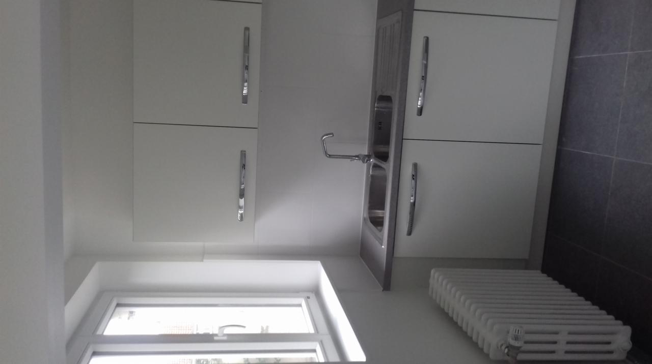 Jasna kuchnia z białymi szafkami, metalowym zlewem i grzejnikiem pod oknem, widok z dołu.