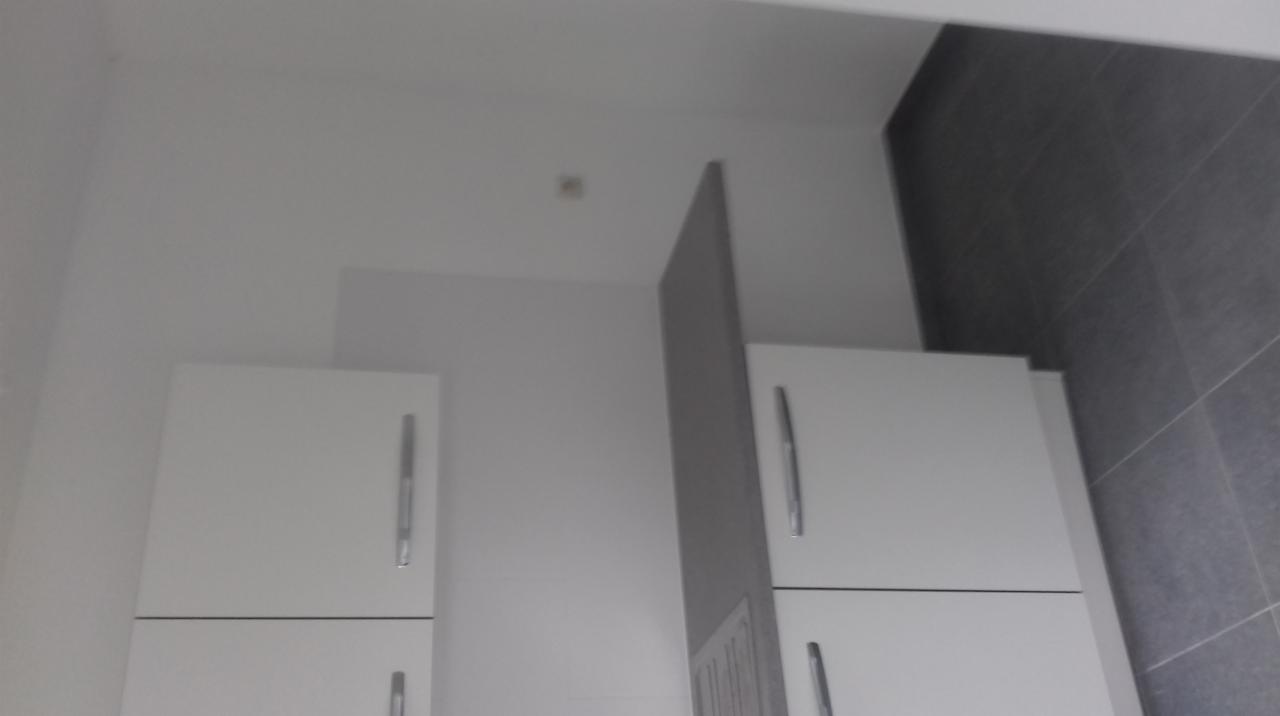 Wykończona kuchnia w Brukseli z białymi szafkami i szarymi płytkami na ścianie, sfotografowana pod kątem.