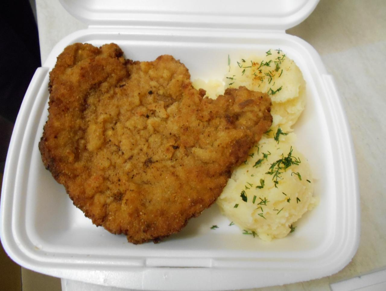 Pojemnik styropianowy z panierowanym kotletem i dwiema porcjami ziemniaków purée posypanych koperkiem.