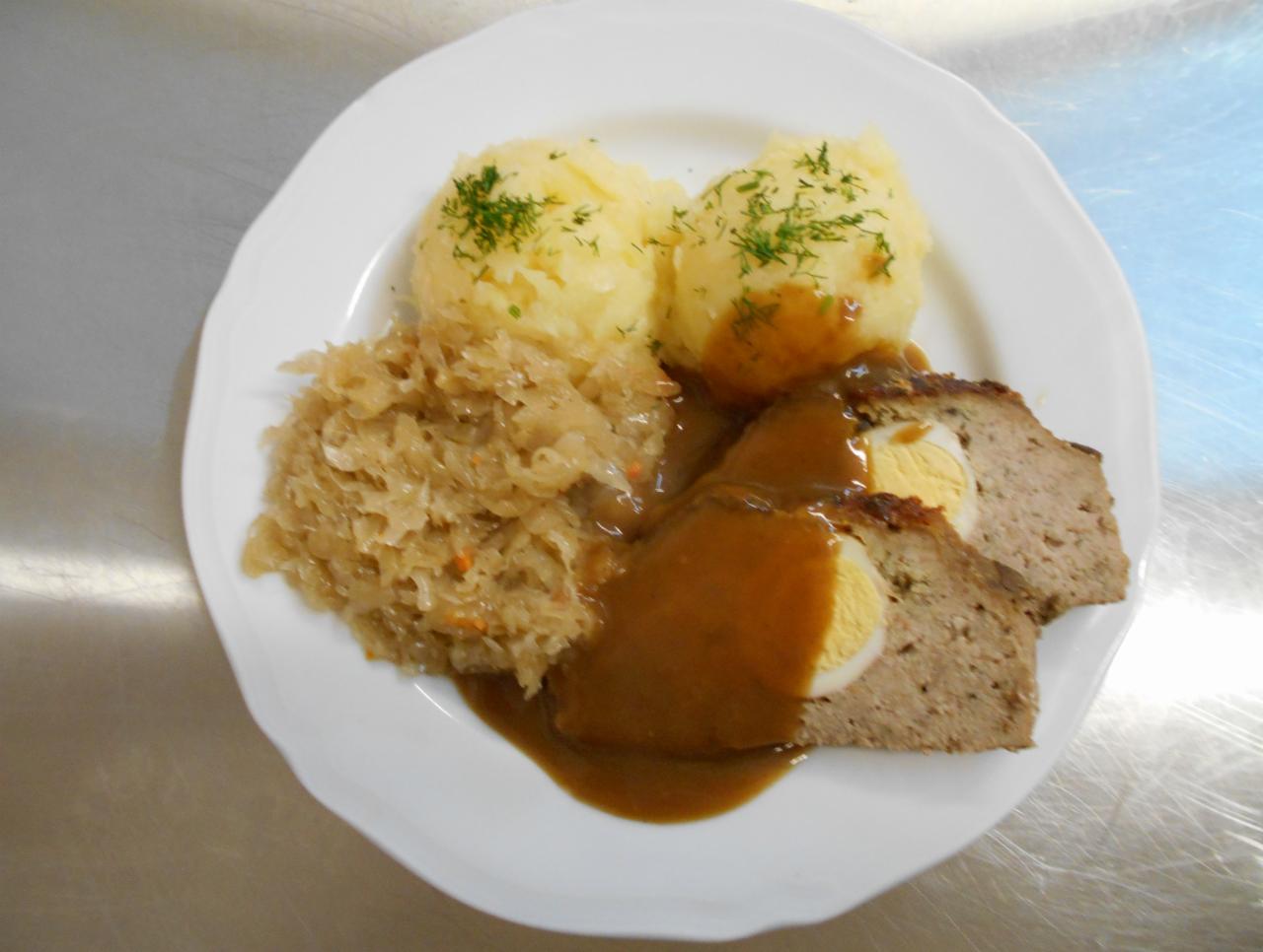 Porcja pieczeni rzymskiej z jajkiem, ziemniakami posypanymi koperkiem i kapustą duszoną, polana sosem na białym talerzu.